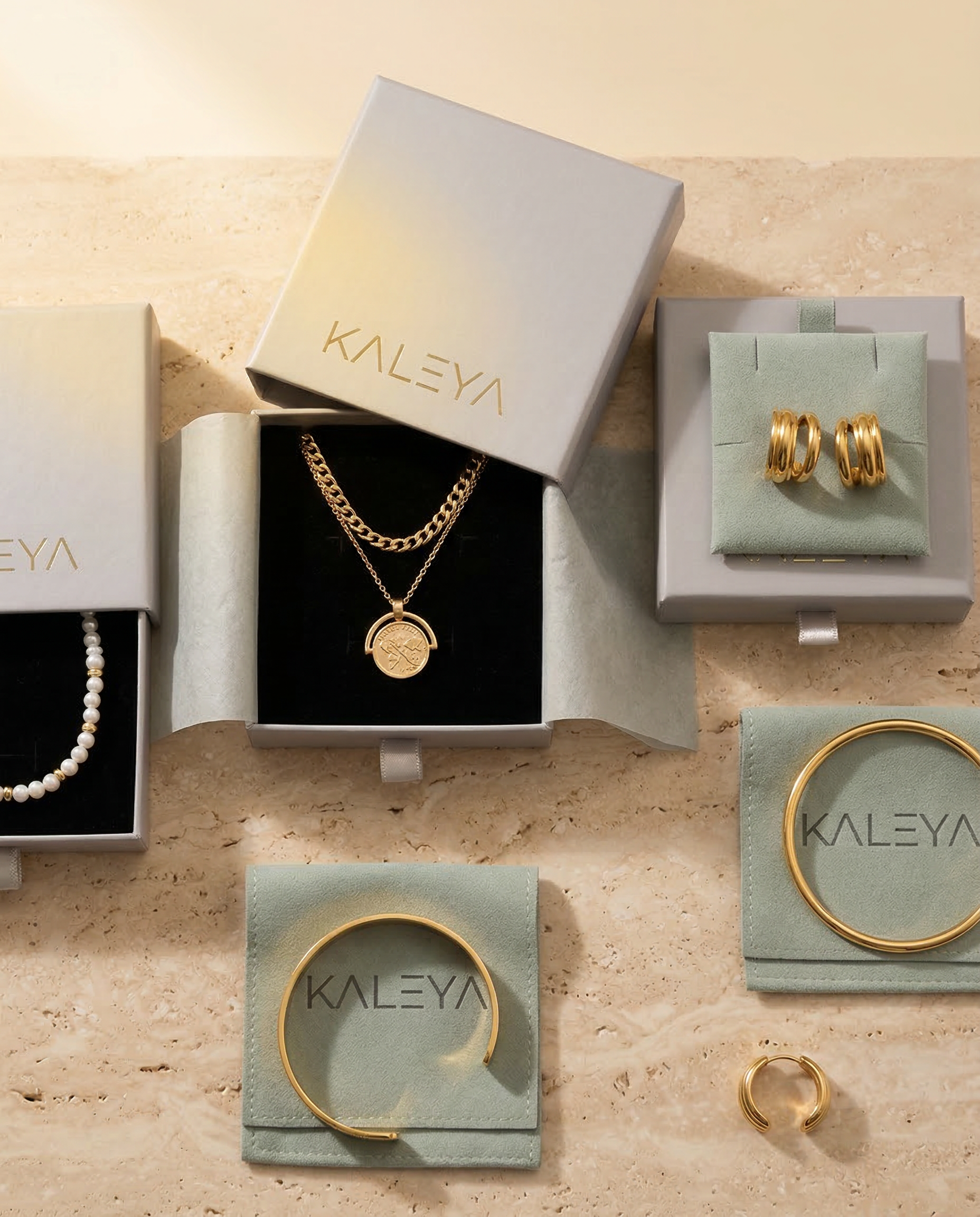 Jewelry set including necklace, bracelet, and earrings in Kaleya boxes on a beige surface.