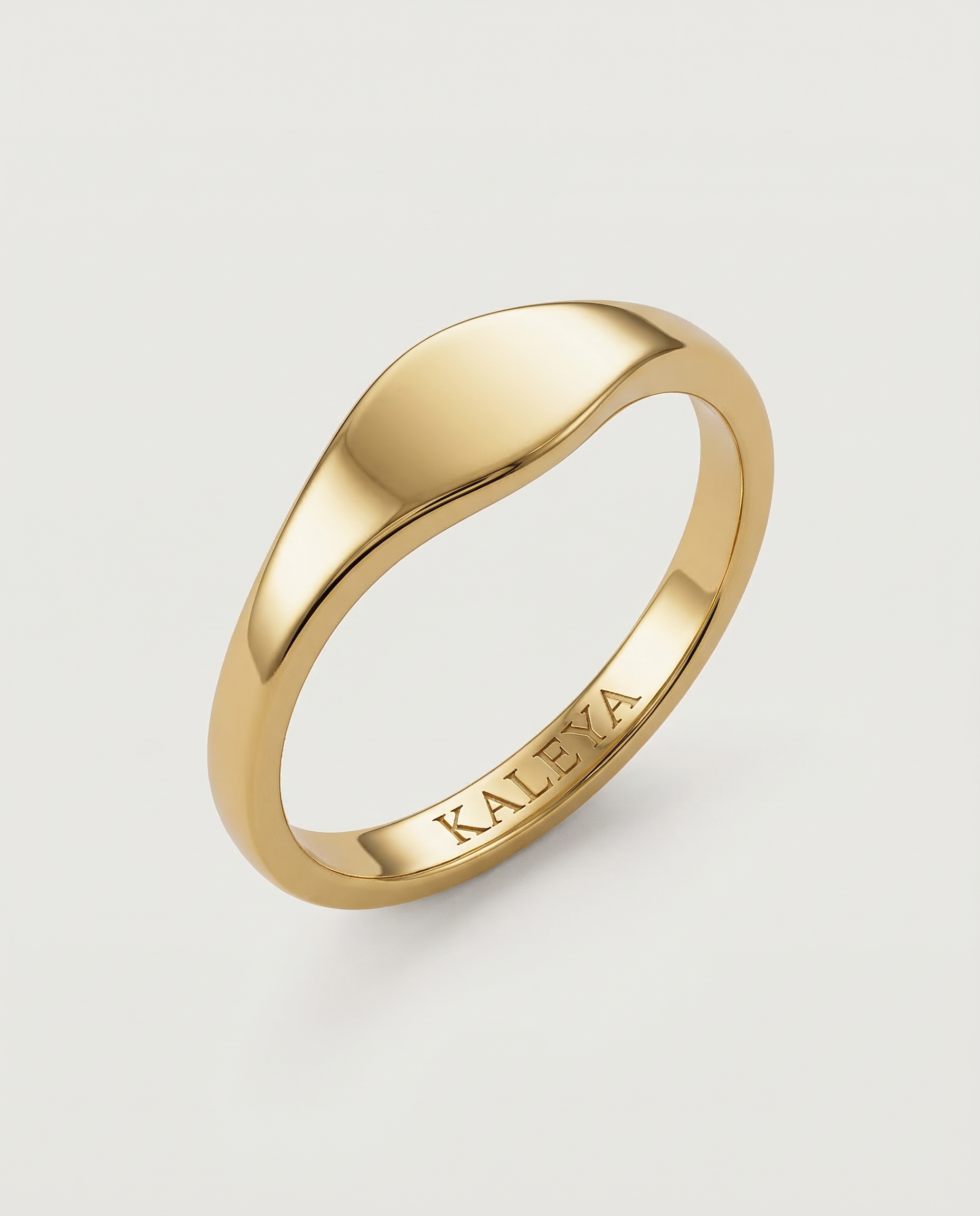 A gold signet ring with a smooth, curved surface on a white background.