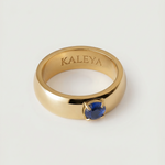 A gold-colored ring with a blue cubic zirconia gemstone in the center, displayed against a white background.