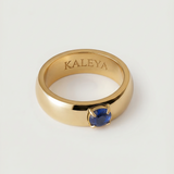 A gold-colored ring with a blue cubic zirconia gemstone in the center, displayed against a white background.