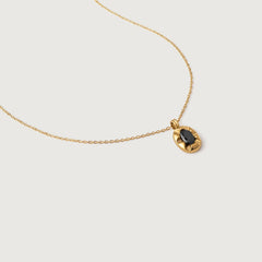 A gold-plated pendant necklace with a black crystal set in a sunburst frame, on a delicate chain.