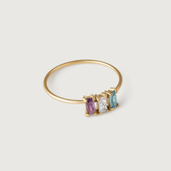 A delicate gold-colored band ring featuring a row of purple, clear, and blue crystals.