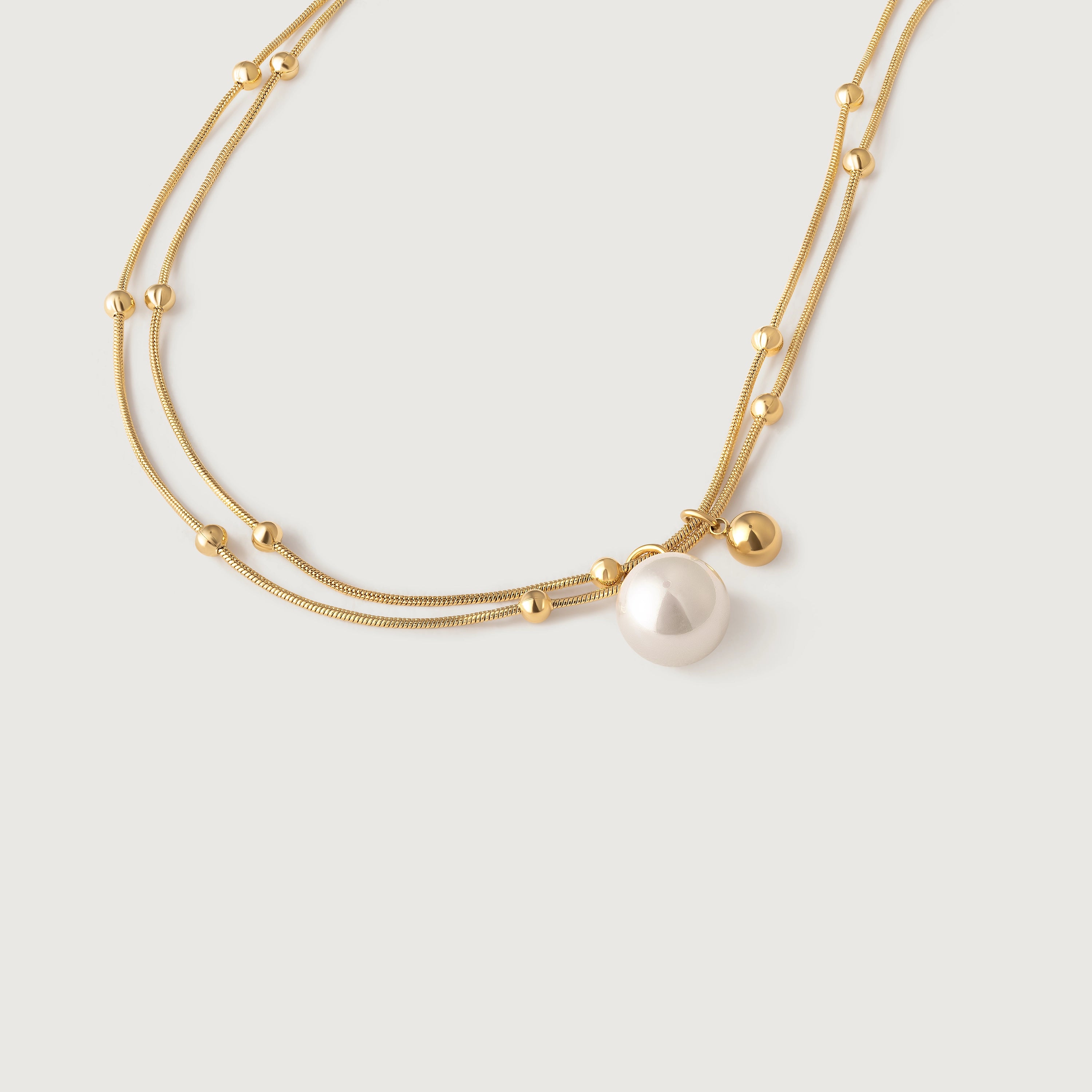 A gold-plated necklace with two parallel chains, studded with tiny golden spheres and featuring a white pearl pendant.