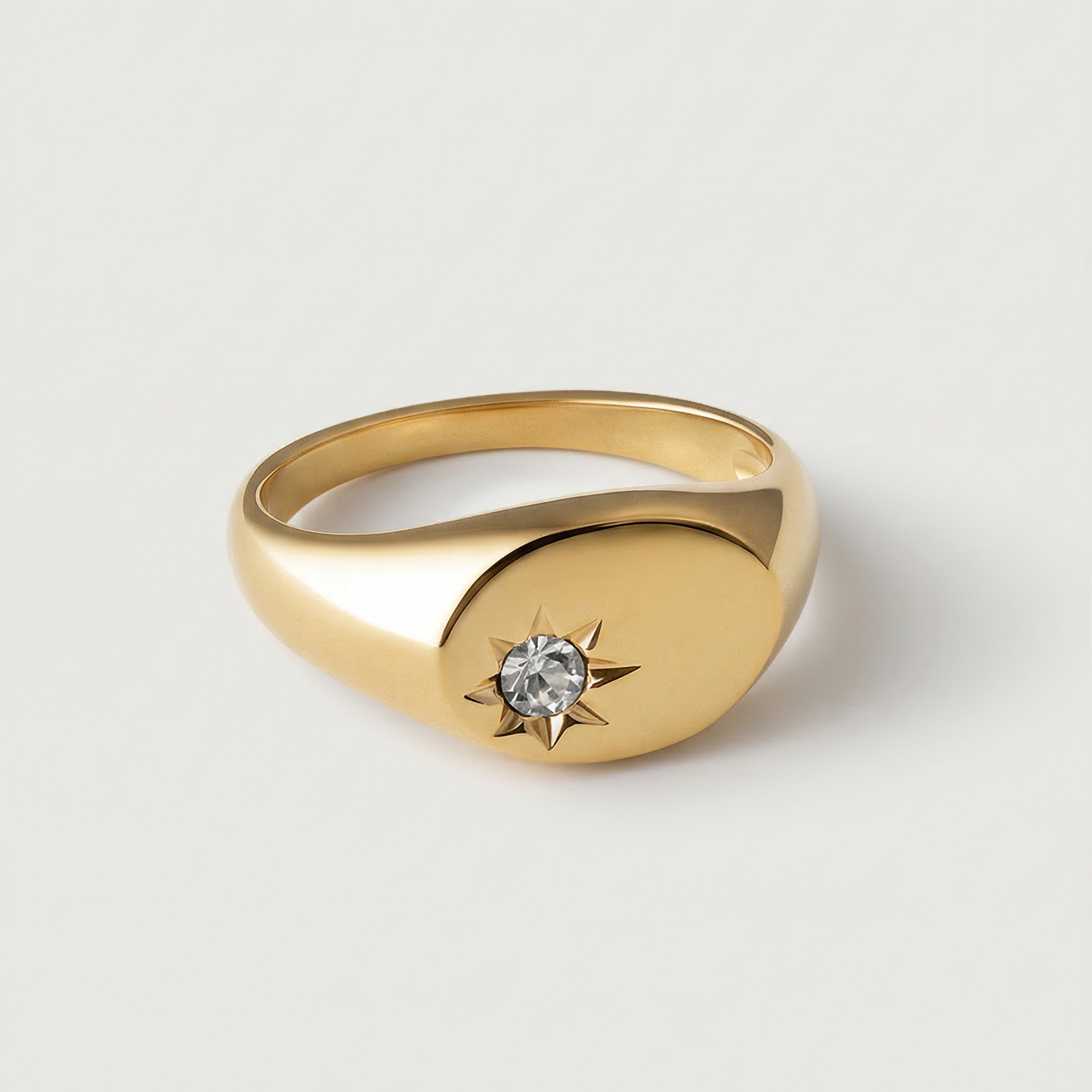 A gold-plated signet ring with an oval face featuring a dazzling stone set in a starburst pattern.