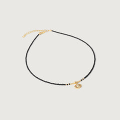 A gold-plated choker necklace with black beads and a crystal-embellished evil eye pendant, featuring an adjustable gold chain.