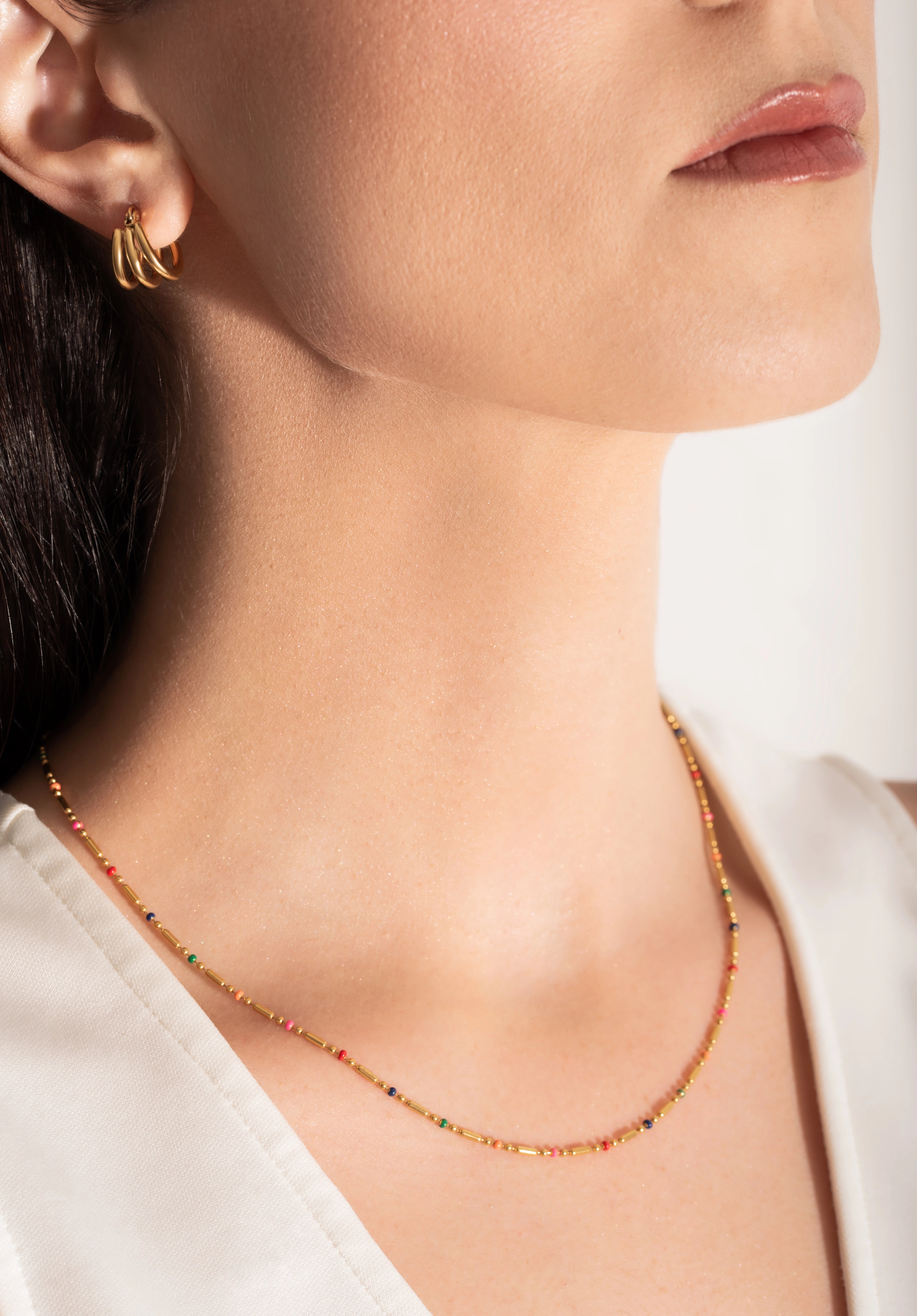 close up of a model wearing a gold-plated necklace with multicolored beads and gold bars