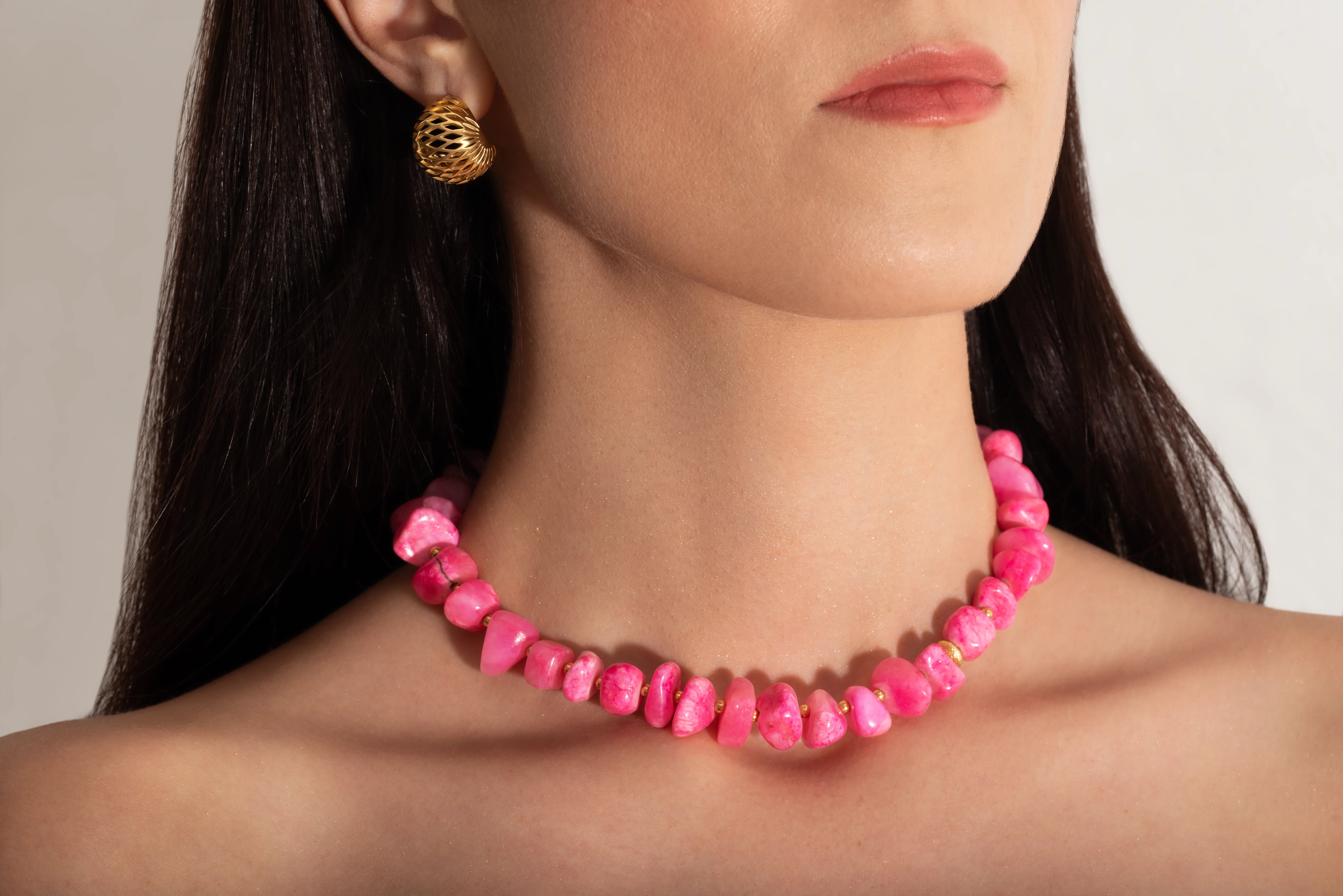 a close up photo of a model wearing a pink coral nuggets necklace with metallic beads and a gold heart charm