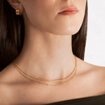 close up of a female model wearing a layered choker necklace with one sleek snake chain and another with tiny spherical stations, both in 18k gold plating.