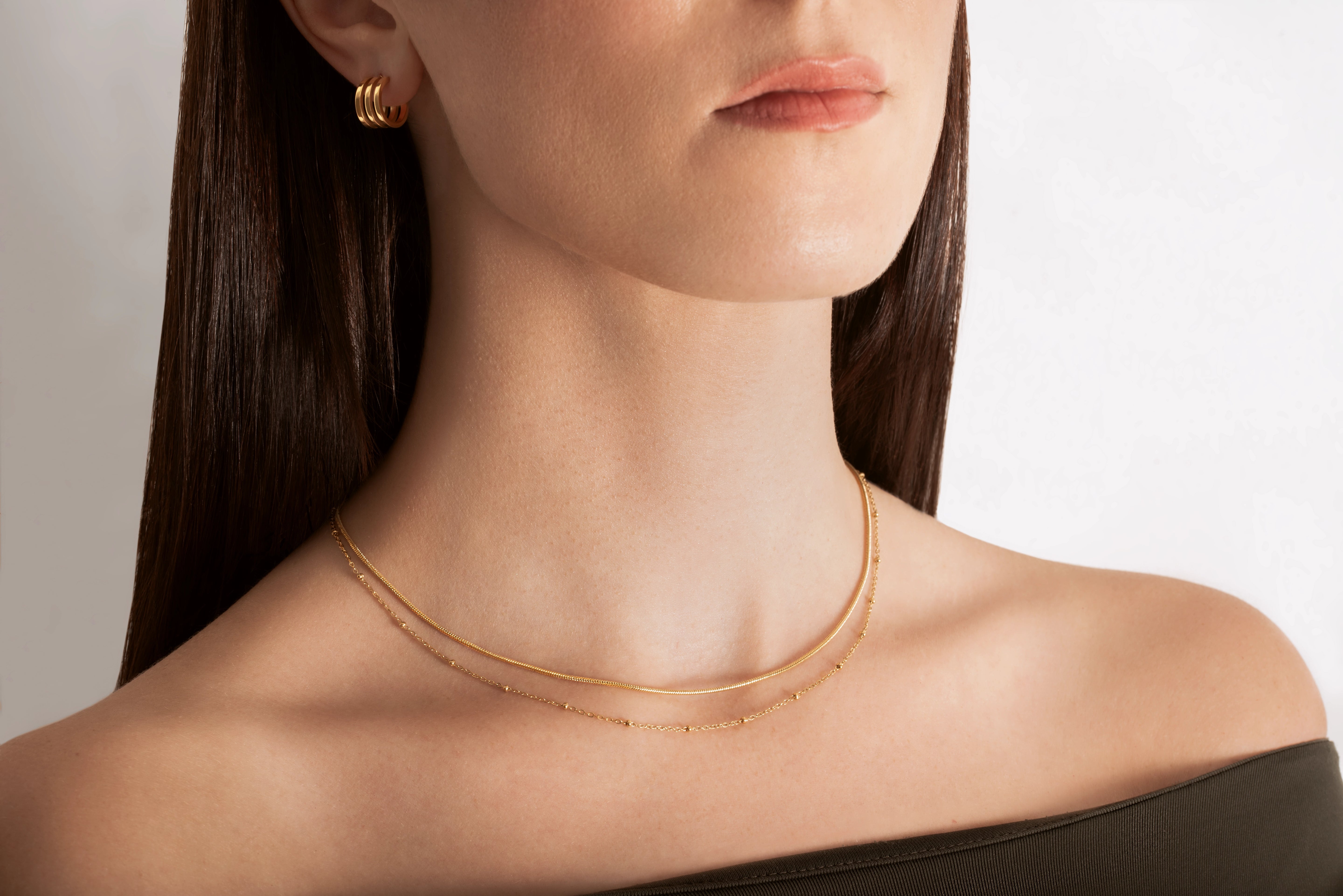 close up of a female model wearing a layered choker necklace with one sleek snake chain and another with tiny spherical stations, both in 18k gold plating.