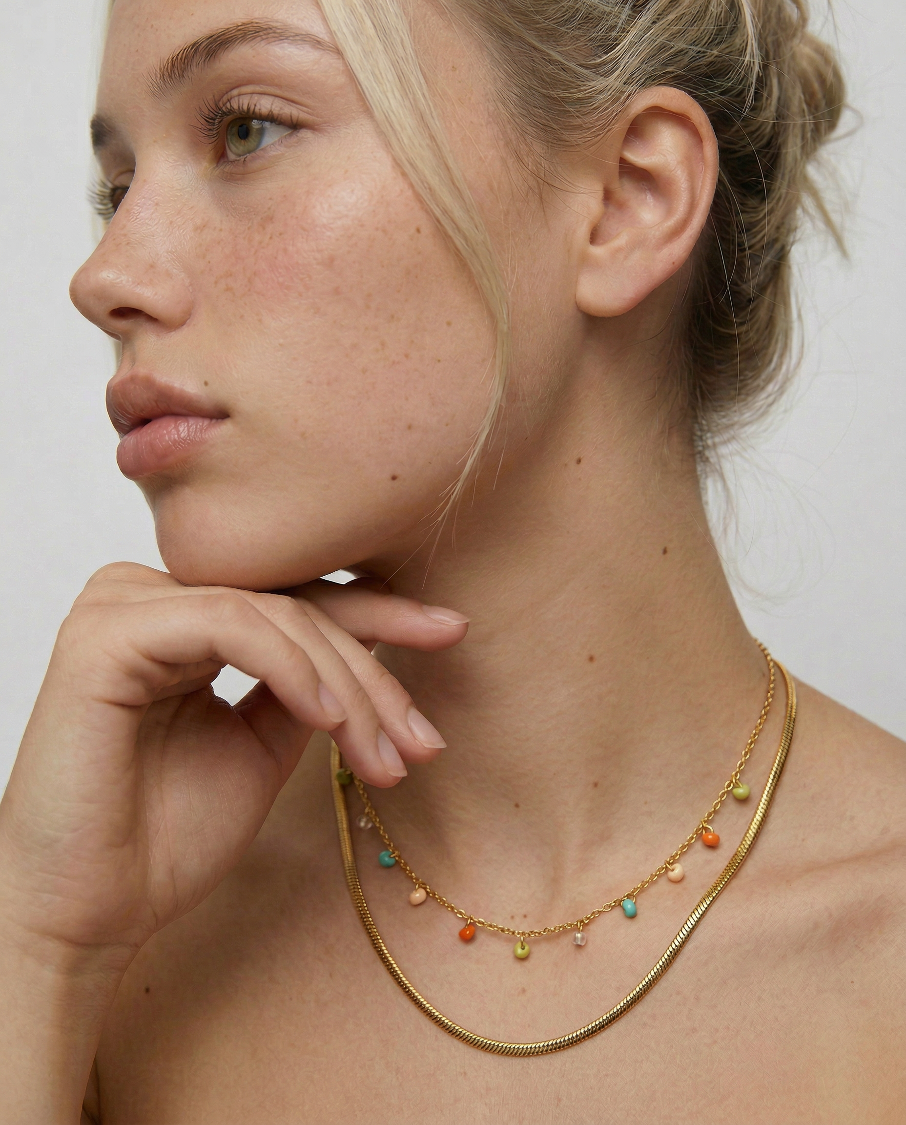 Woman wearing a gold necklace with colorful beads against a neutral background