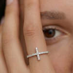 model wearing a silver ring with a delicate cross adorned with sparkling diamonds on the top, set on a slender band with pave-set diamonds
