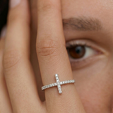 model wearing a silver ring with a delicate cross adorned with sparkling diamonds on the top, set on a slender band with pave-set diamonds