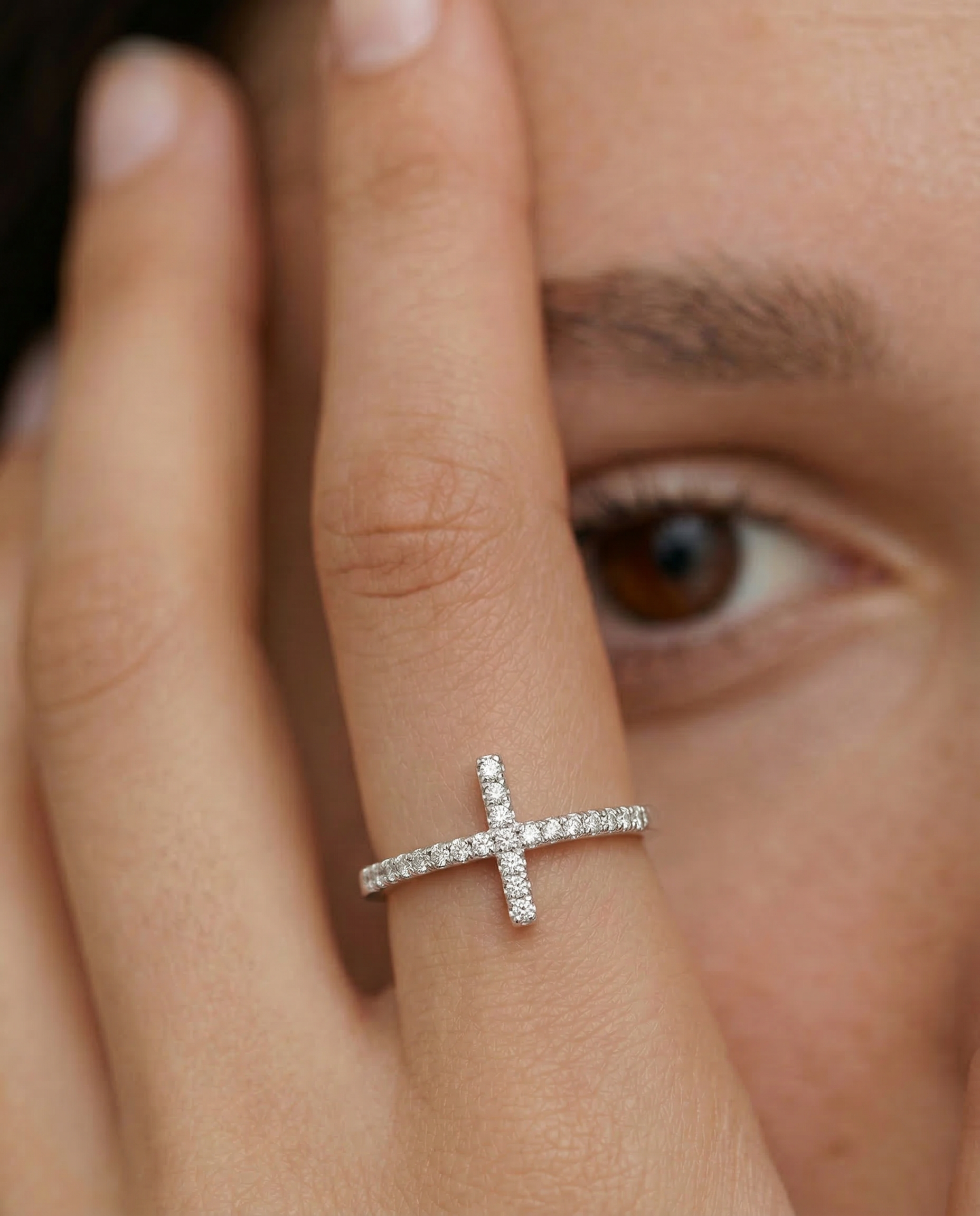 model wearing a silver ring with a delicate cross adorned with sparkling diamonds on the top, set on a slender band with pave-set diamonds
