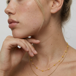 Woman wearing a delicate gold necklace with a plain background