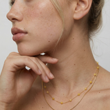 Woman wearing a delicate gold necklace with a plain background