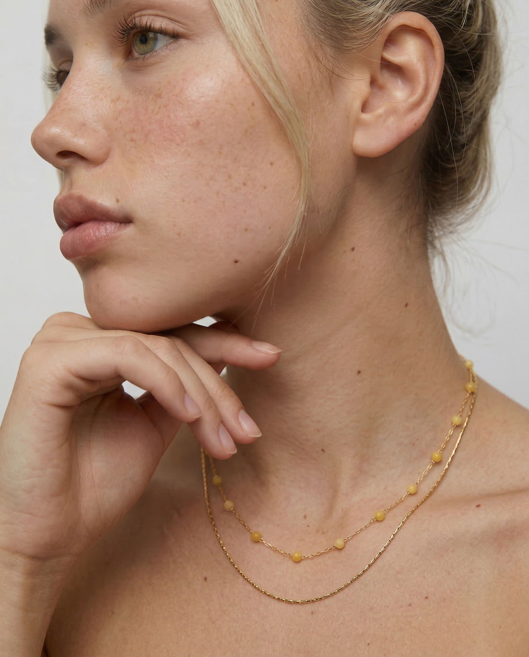 Woman wearing a delicate gold necklace with a plain background