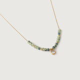 A gold-plated necklace with sage-green faceted crystals and a gold spacer bead chain, ending in a cubic zirconia charm.