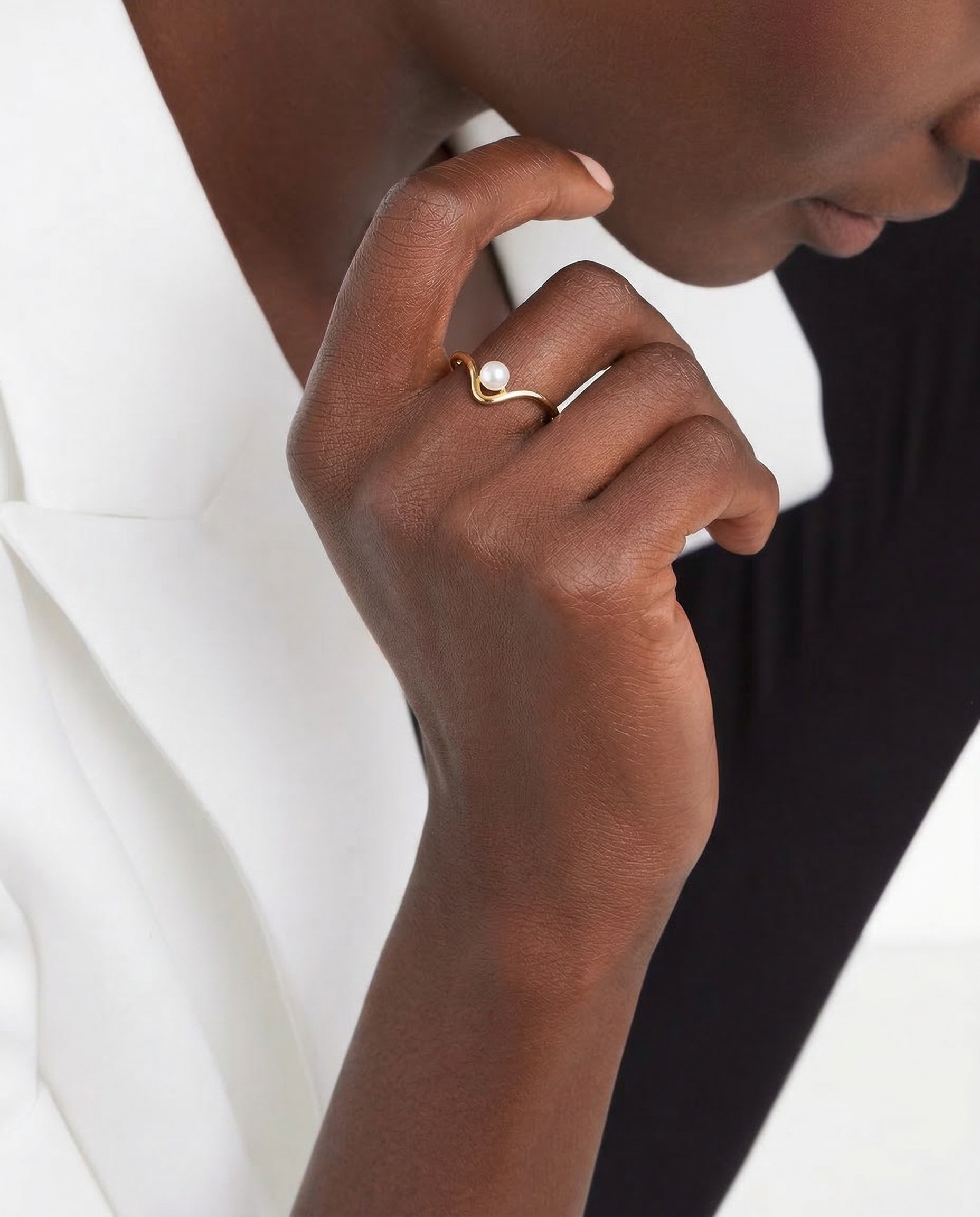 Close-up of a hand wearing a gold ring with a white stone on a neutral background