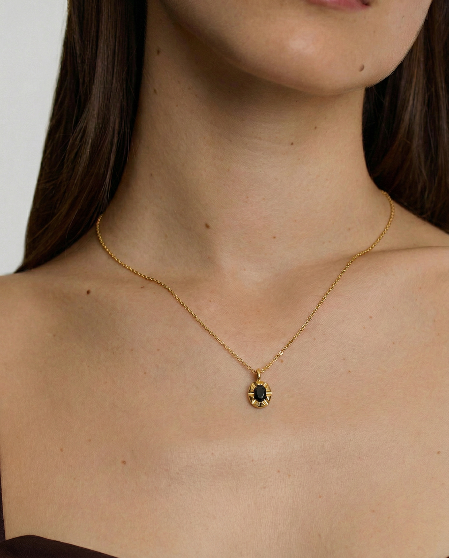 model wearing a gold-plated pendant necklace with a black crystal set in a sunburst frame