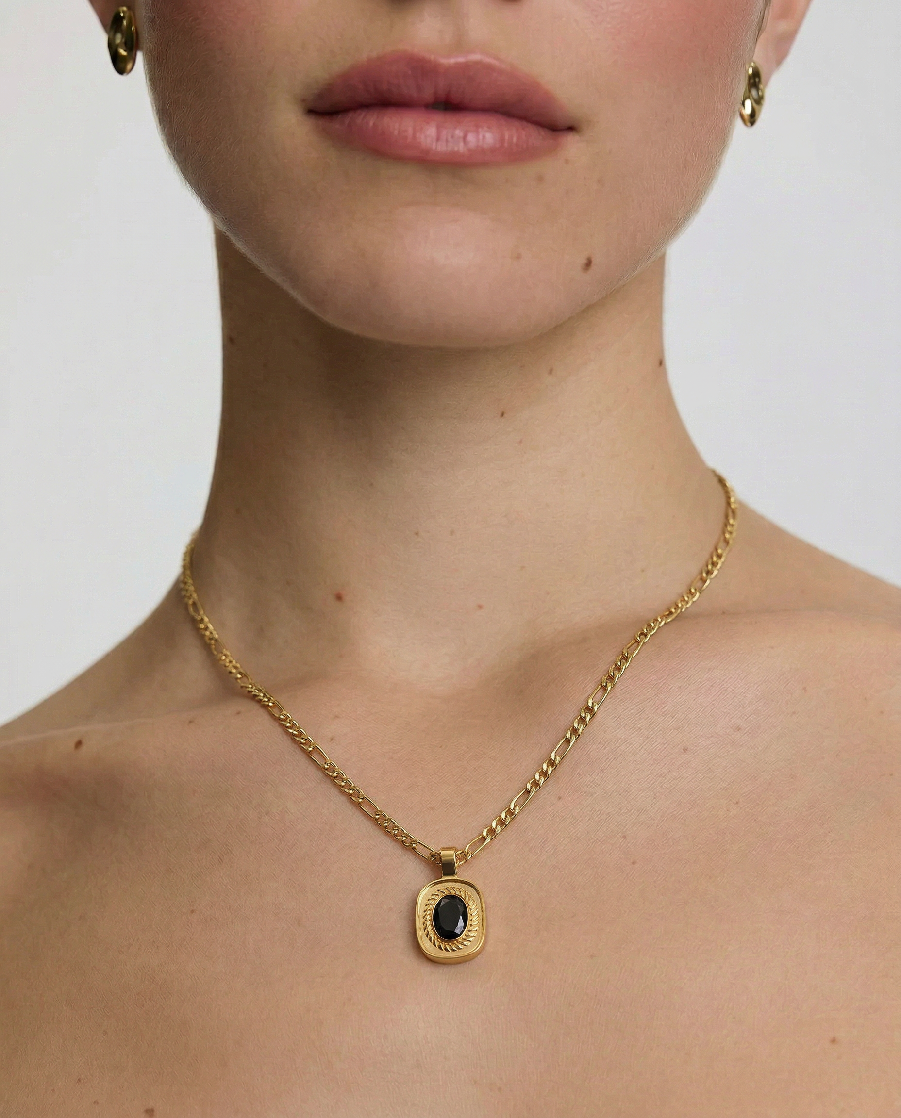 Close-up of a person wearing a gold necklace with a black pendant on a plain background