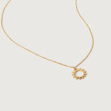 A gold necklace with a minimalist sun charm pendant on a white background.