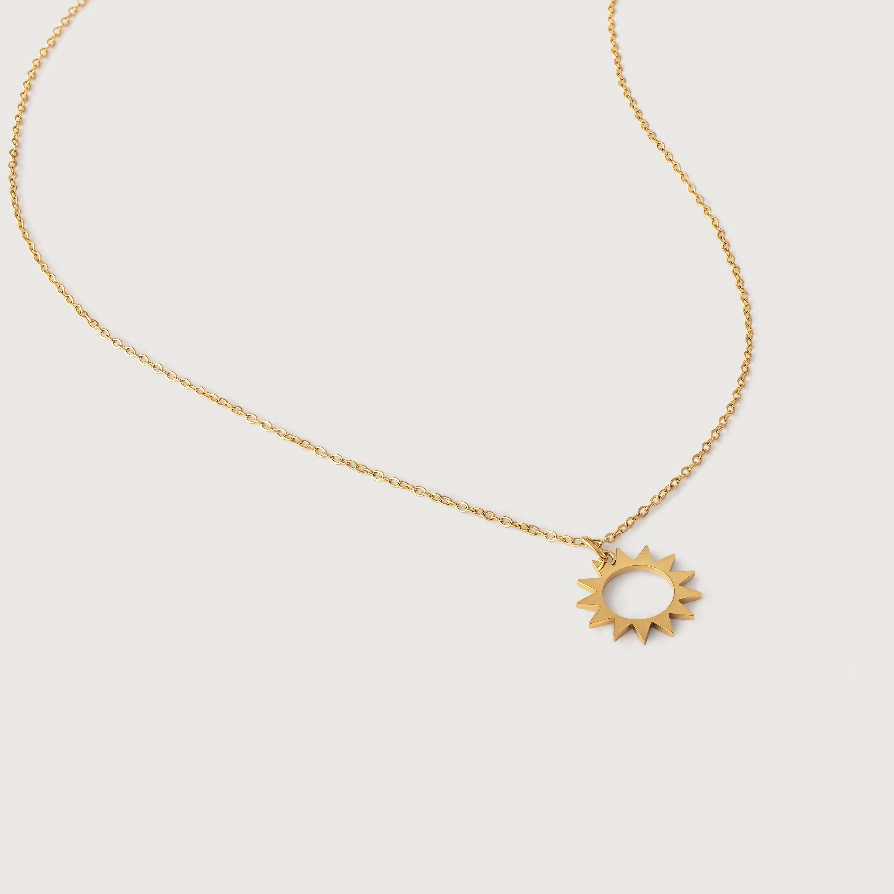 A gold necklace with a minimalist sun charm pendant on a white background.