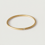 A gold-colored band ring with a single sparkling stone on a white background.