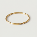 A gold-colored band ring with a single sparkling stone on a white background.