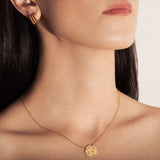 studio model wearing a gold-plated necklace with a round medallion pendant