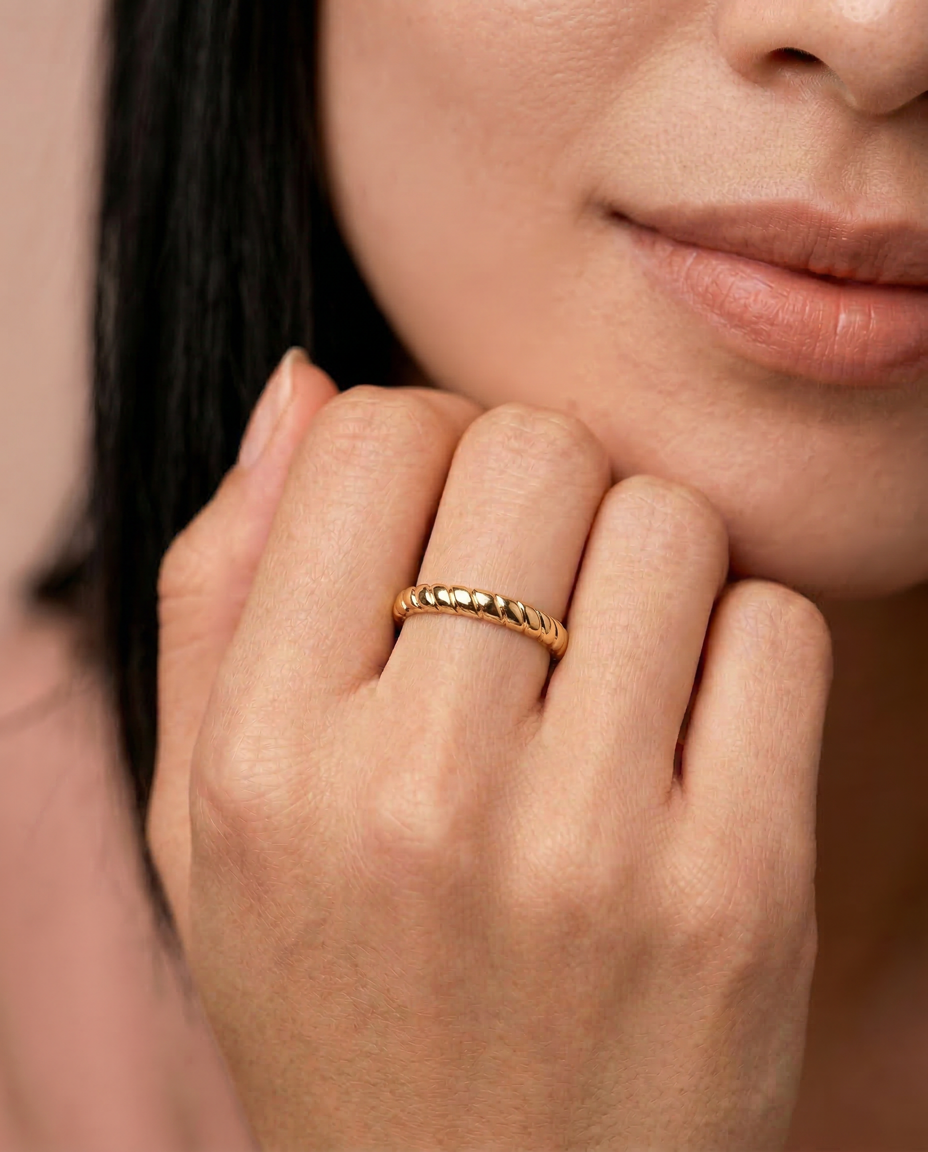 model wearing a gold-plated metal ring with a twisted rope design, displayed against a white background.
