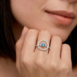 Close-up of a woman's hand wearing a sleek sterling silver ring with a single blue gemstone in the center, set within a circular frame.