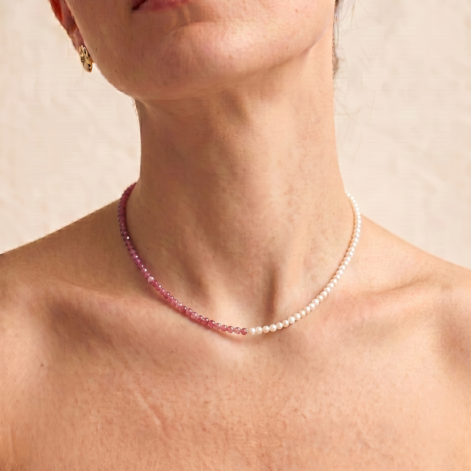 close up of a model wearing  a Rose quartz and pearl beaded necklace in gold, with one half strung with imitation pearl rice beads and the other half with faceted rose quartz beads graduating from soft blush to deep pink.