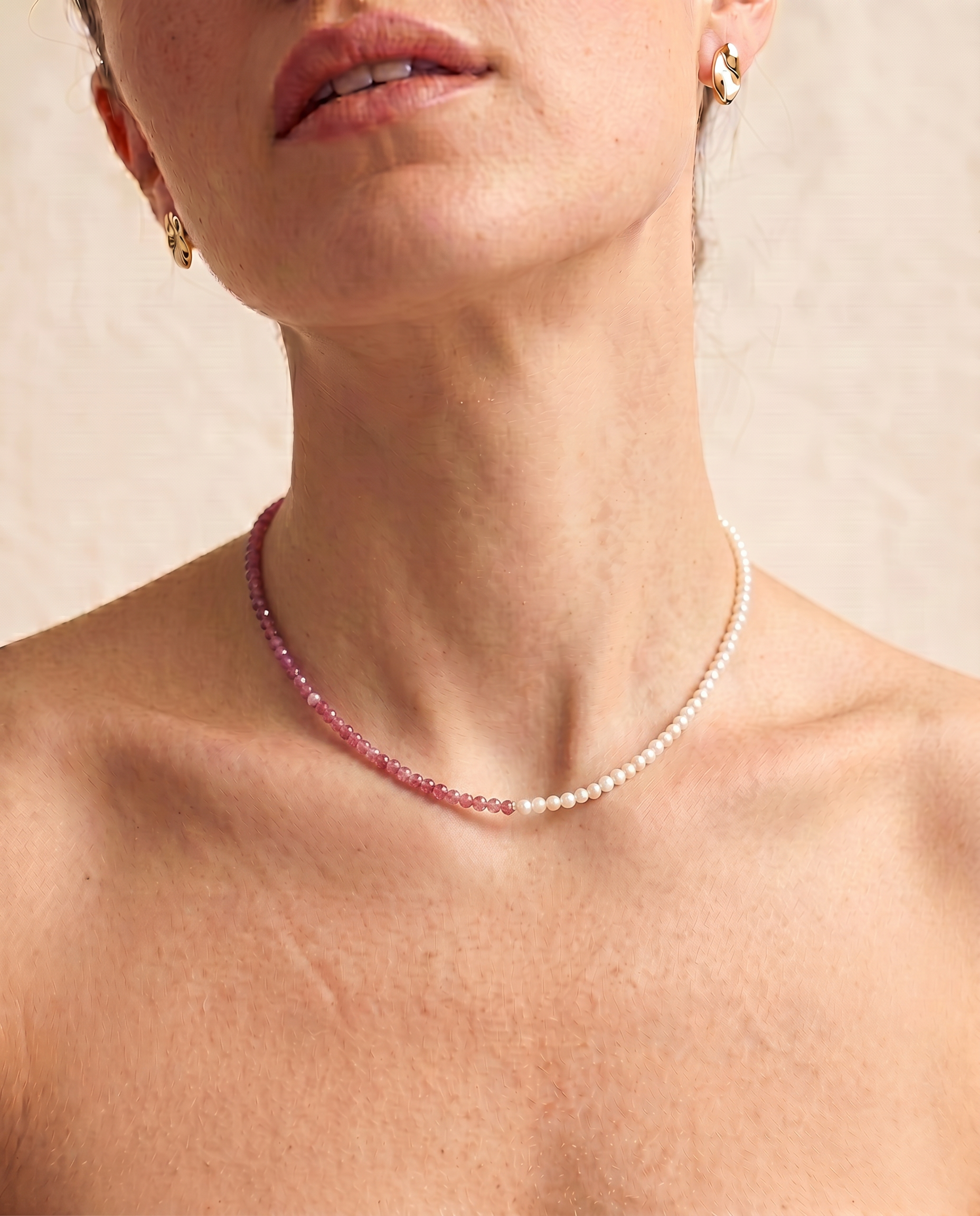 close up of a model wearing  a Rose quartz and pearl beaded necklace in gold, with one half strung with imitation pearl rice beads and the other half with faceted rose quartz beads graduating from soft blush to deep pink.