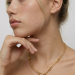 Woman wearing a gold necklace with a pearl pendant against a plain background