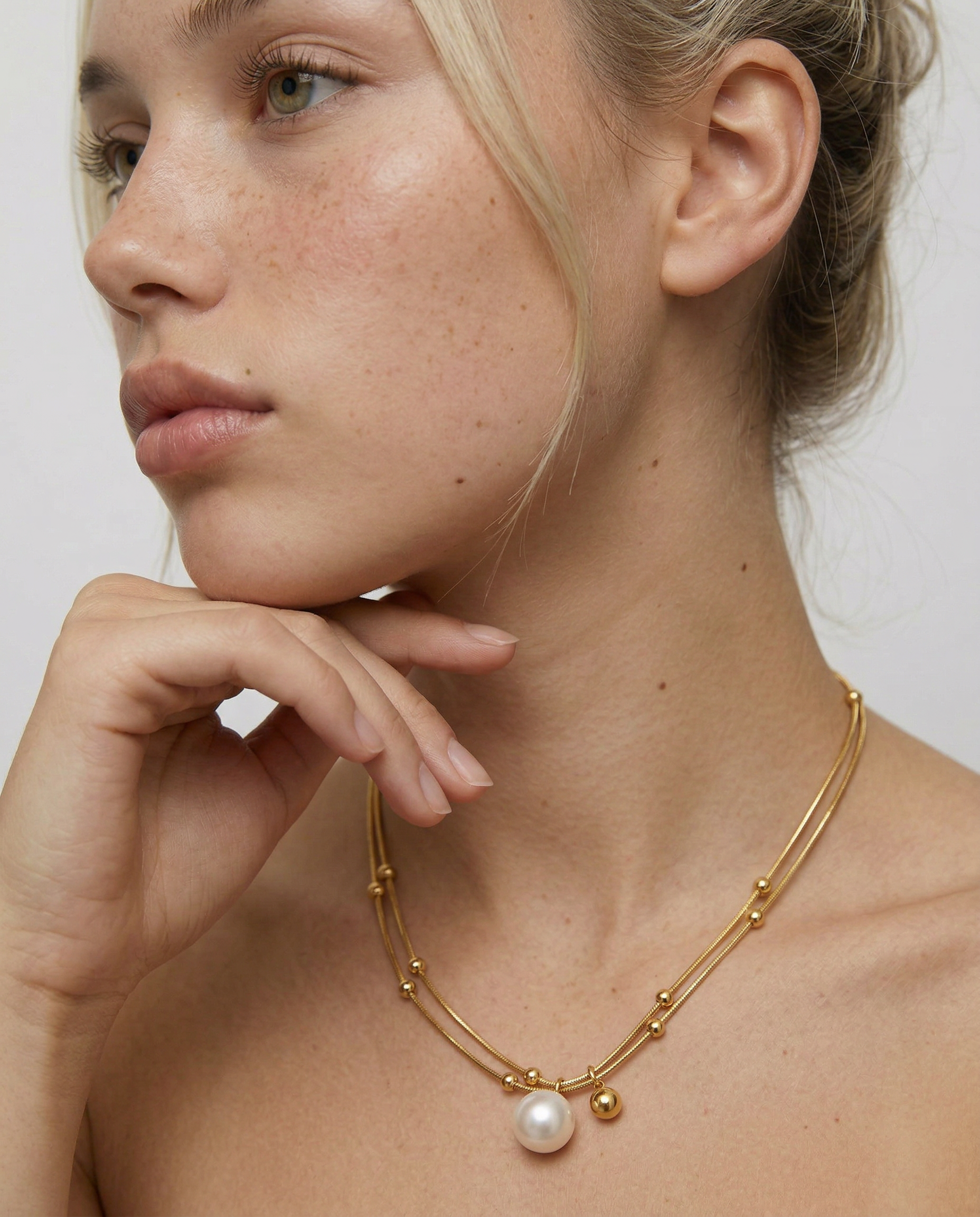 Woman wearing a gold necklace with a pearl pendant against a plain background