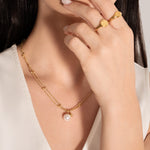 model wearing a gold-plated necklace with two parallel chains, studded with tiny golden spheres and featuring a white pearl pendant.