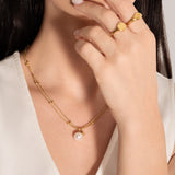 model wearing a gold-plated necklace with two parallel chains, studded with tiny golden spheres and featuring a white pearl pendant.