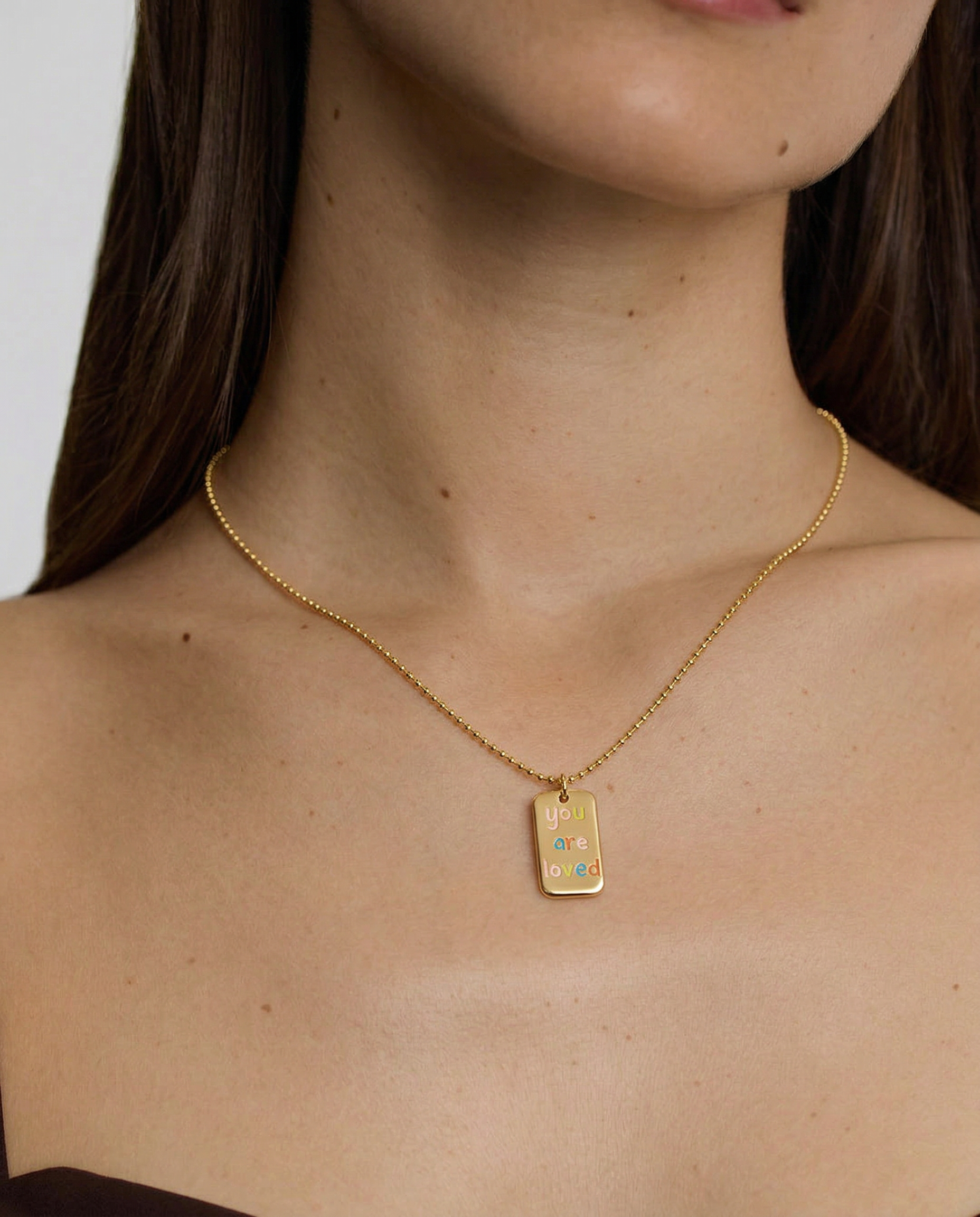 Gold necklace with a rectangular pendant worn by a person