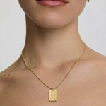 model wearing a gold-plated necklace with a polished rectangular tag pendant featuring the phrase 'you are loved' in rainbow enamel letters, attached to a ball chain.