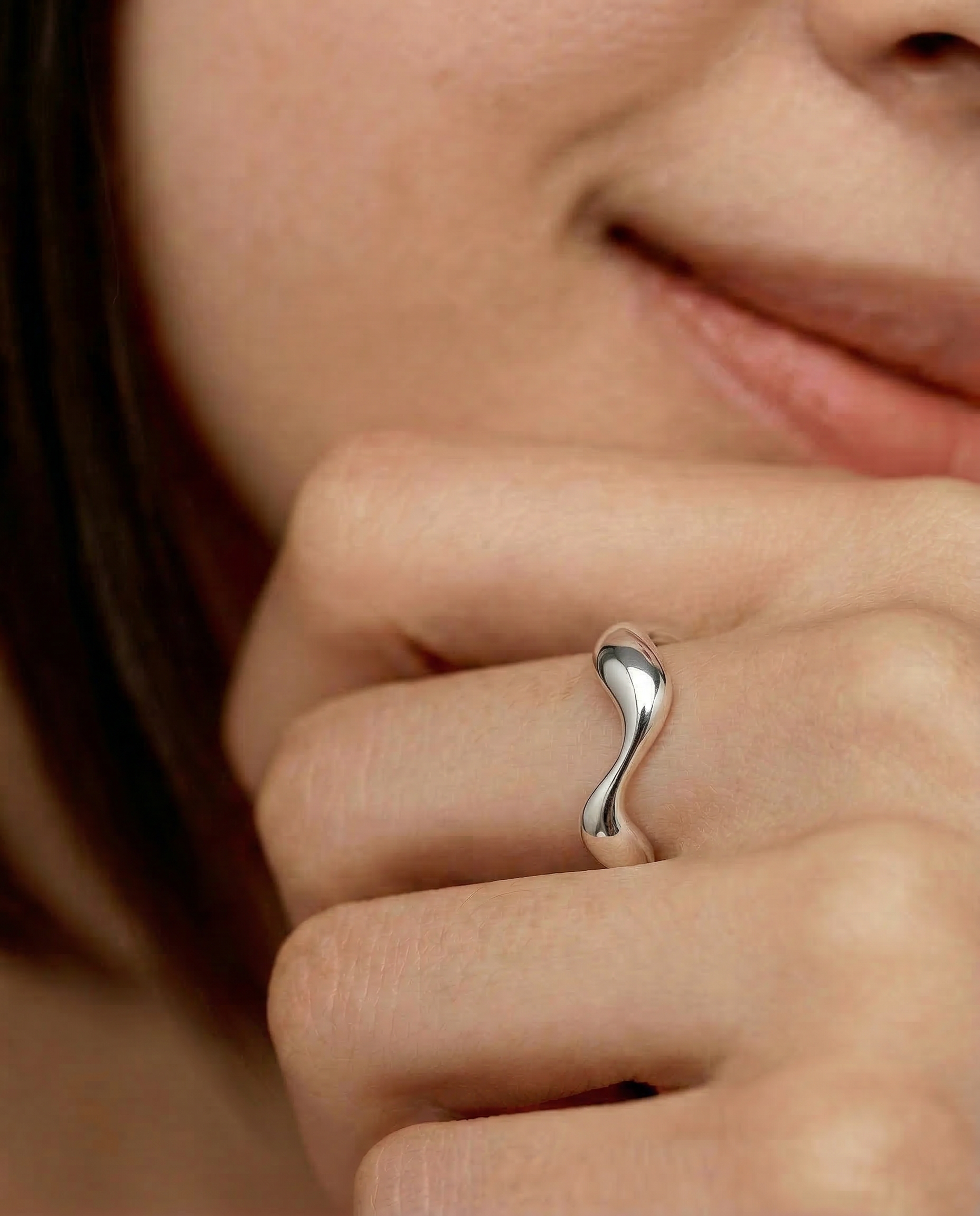 close up of a female model wearing a sleek silver ring with an undulating design, crafted from sterling silver