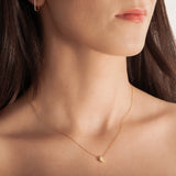 model wearing a delicate gold-plated necklace with a hexagonal setting and a single crystal pendant.