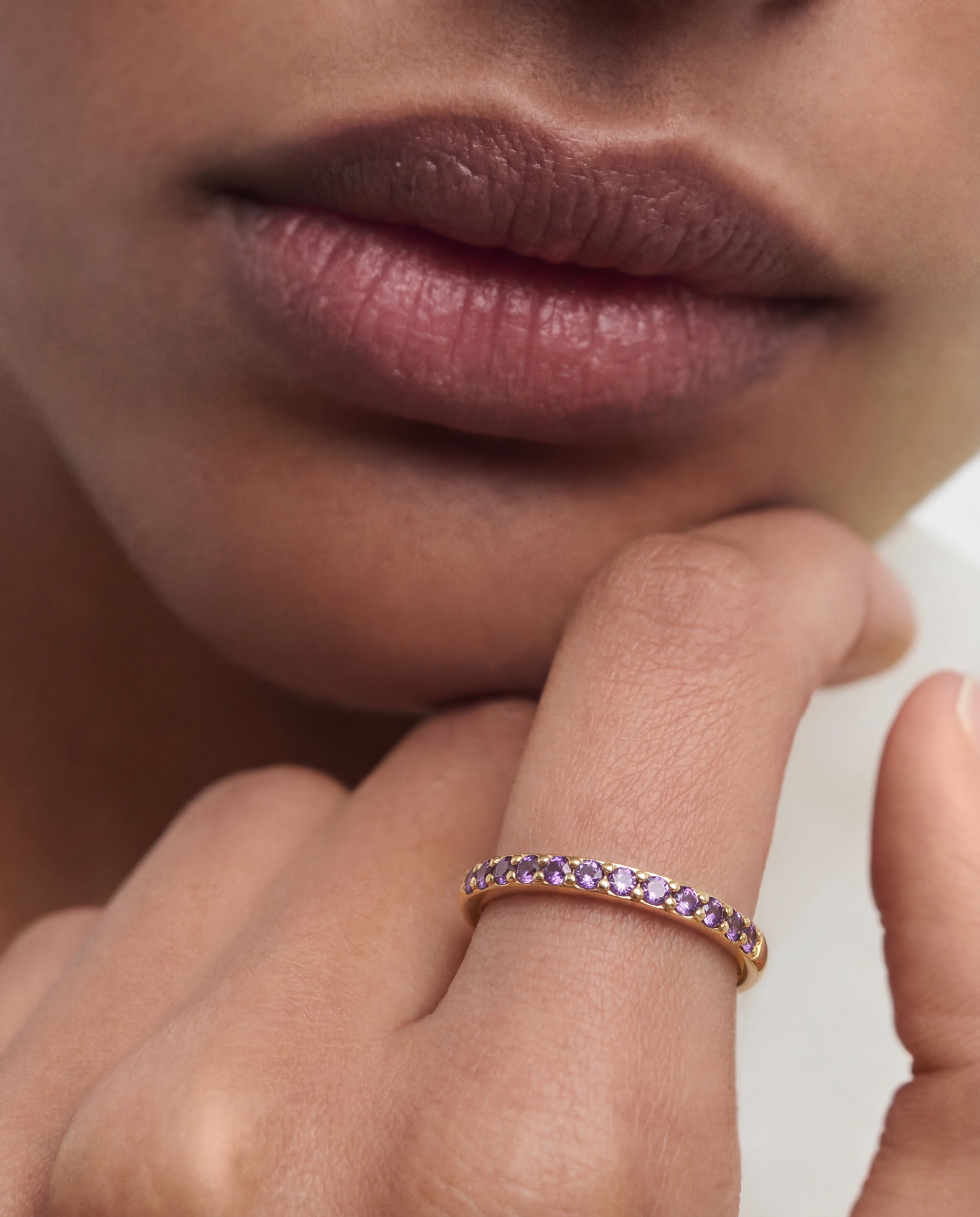 Close-up of a hand wearing a rose gold ring with purple gemstones, resting on a blurred background.
