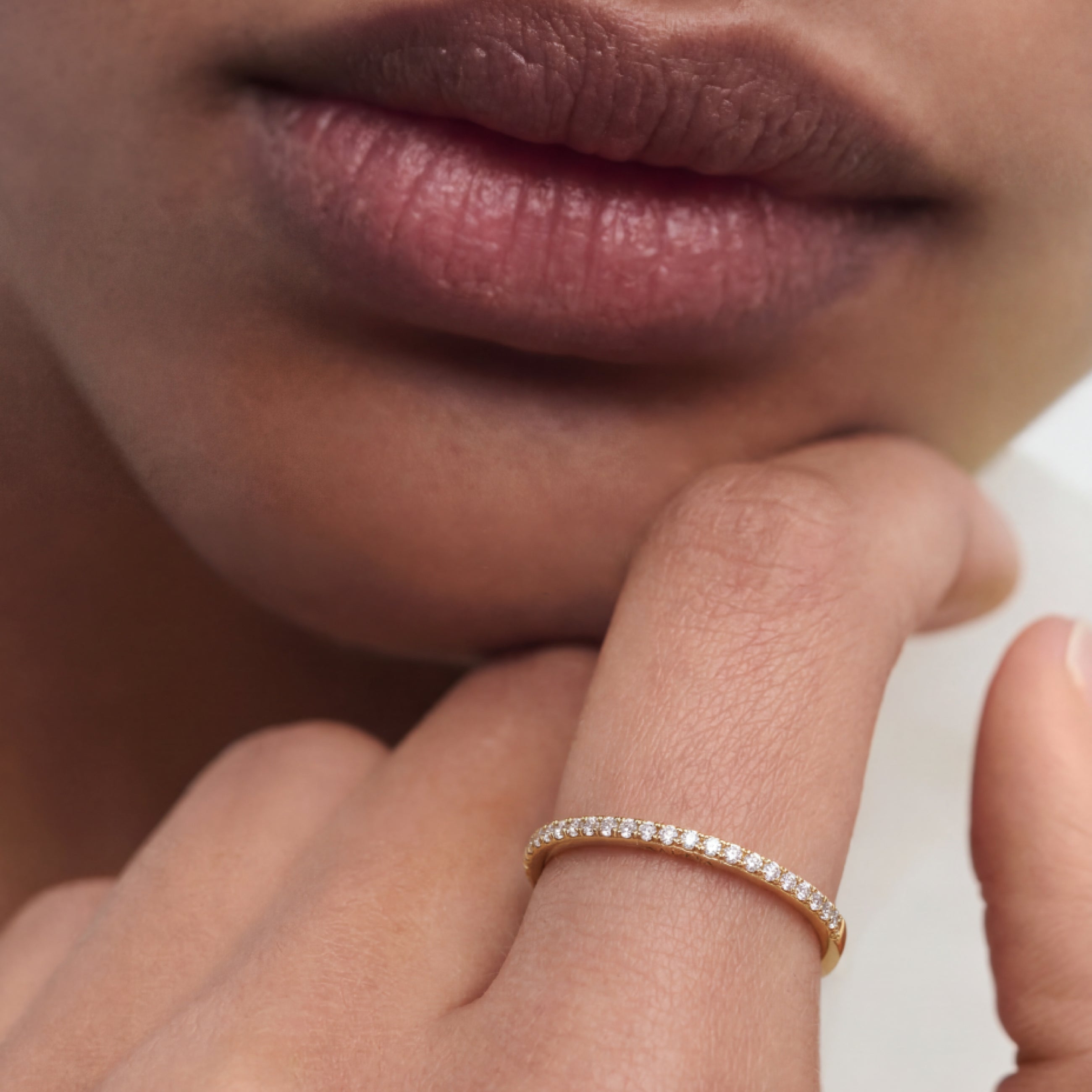 Close-up of a person's hand with a gold ring on a neutral background