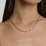 female model wearing a gold-plated necklace with multicolored beads in red, pink, blue, and green, arranged in a alternating pattern between golden bars.