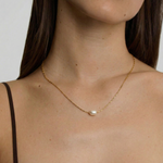 Woman wearing a delicate gold necklace with a pearl pendant against a neutral background