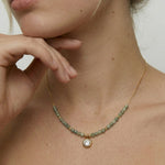 model wearing a gold-plated necklace with sage-green faceted crystals and cubic zirconia charm.