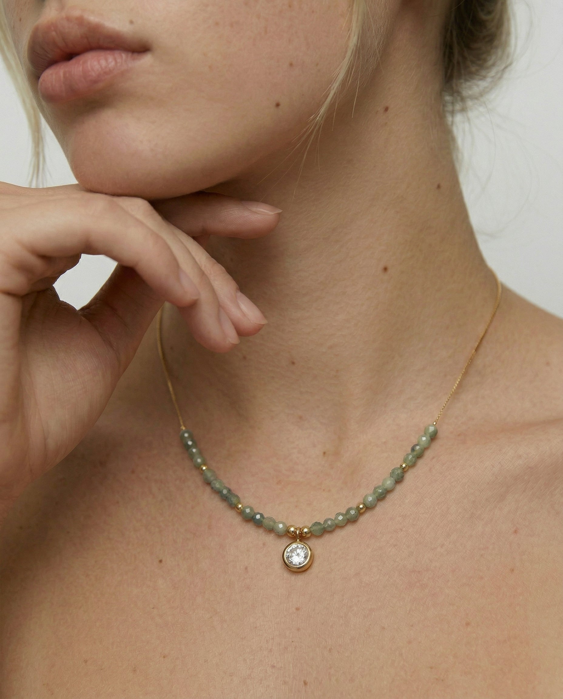 model wearing a gold-plated necklace with sage-green faceted crystals and cubic zirconia charm.