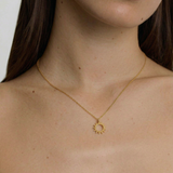 female model wearing a gold necklace with a minimalist sun charm pendant