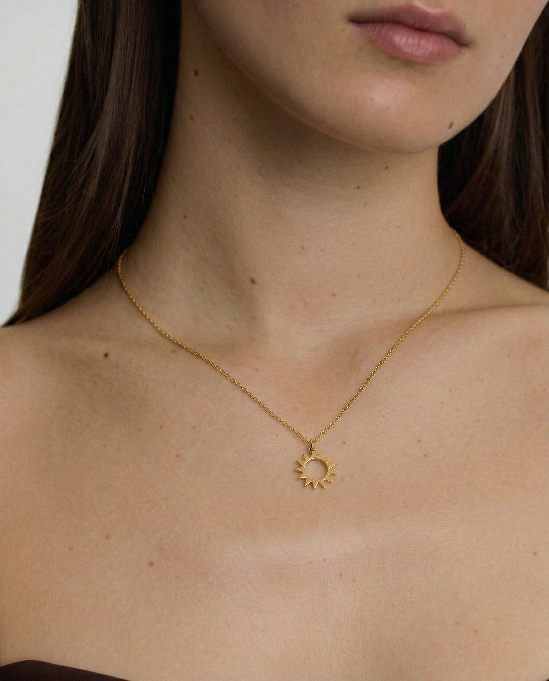 female model wearing a gold necklace with a minimalist sun charm pendant