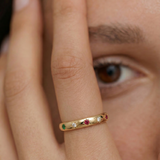 model wearing a gold-plated ring with a series of vibrant gemstones set in star-shaped bezels along the polished band